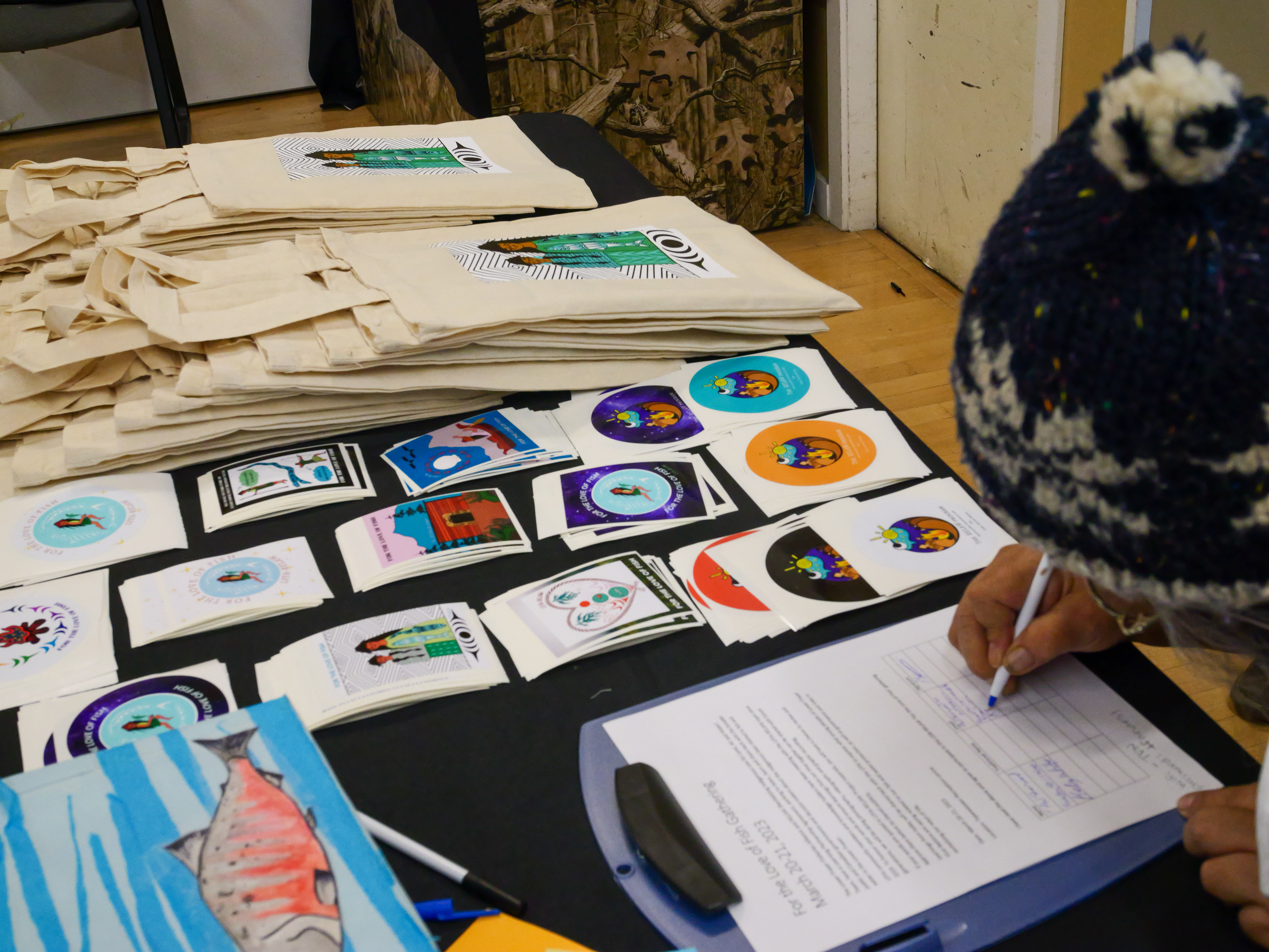 A participant fills out a signup sheet at a table covered with stickers and swag