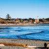 Pebble beach and shoreline with structures and a lighthouse in the distance